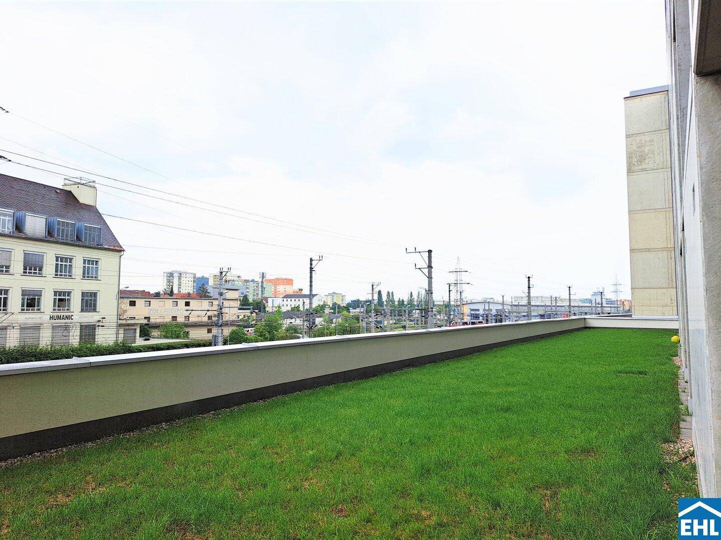 Grüne Dachfläche mit Rasen und Blick auf die Stadt und Bahngleise unter bewölktem Himmel.