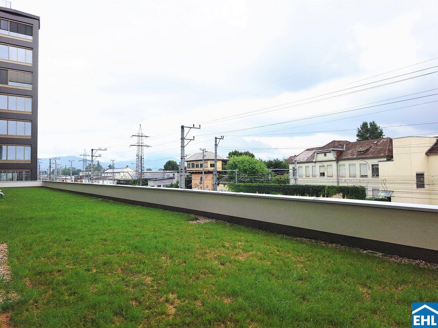 Rasenfläche auf einer erhöhten Plattform mit Blick auf Wohngebäude und Bahngleise.