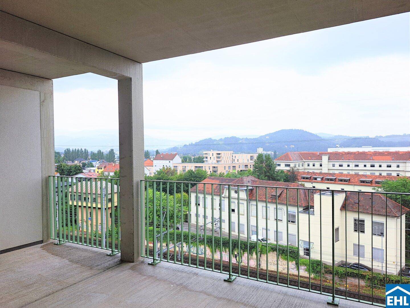 Geräumiger Betonbalkon mit grüner Brüstung und weitem Blick über die Stadt und Hügel.