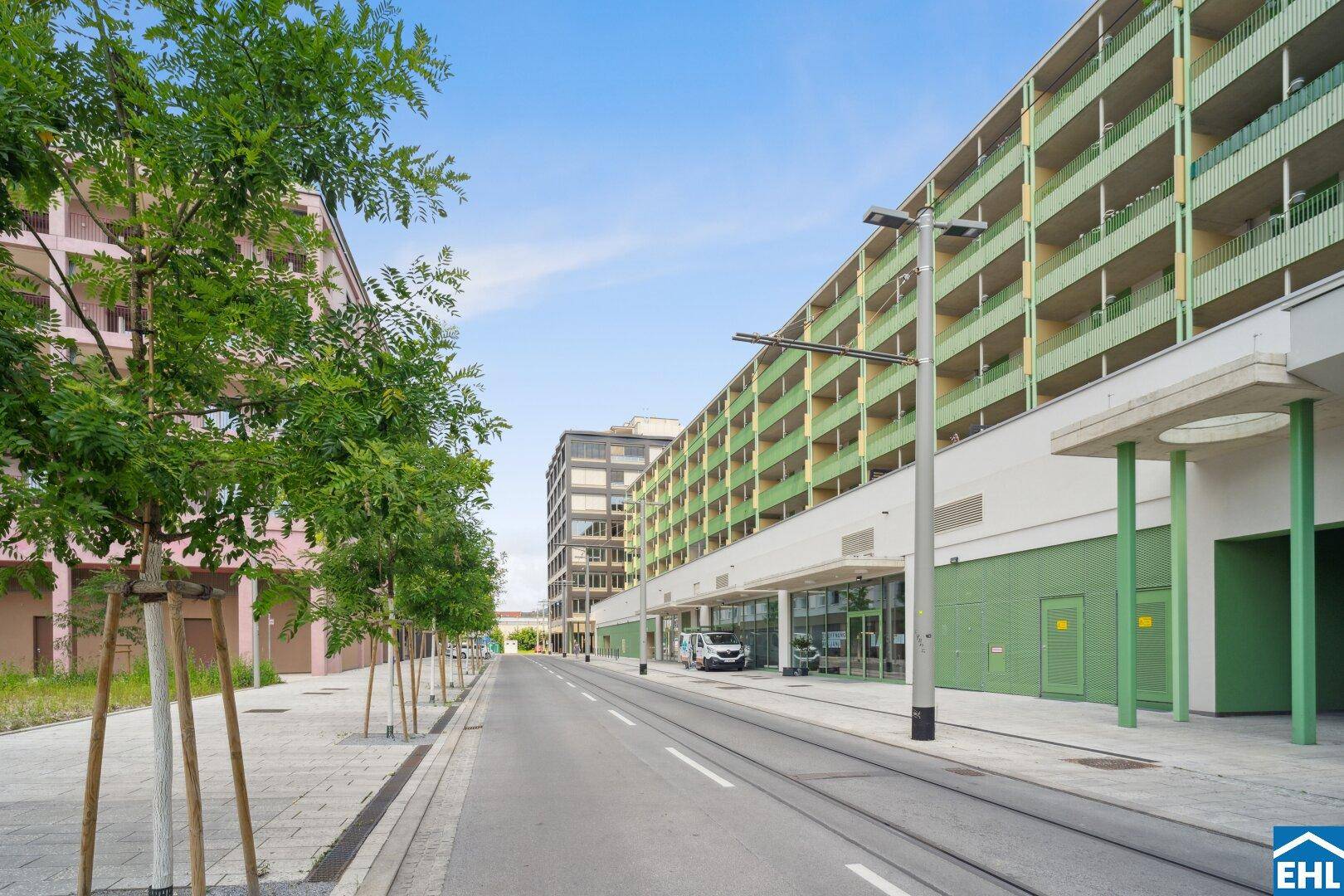 Moderne Wohngebäude entlang einer Straße mit Straßenbahnschienen und viel Grün.