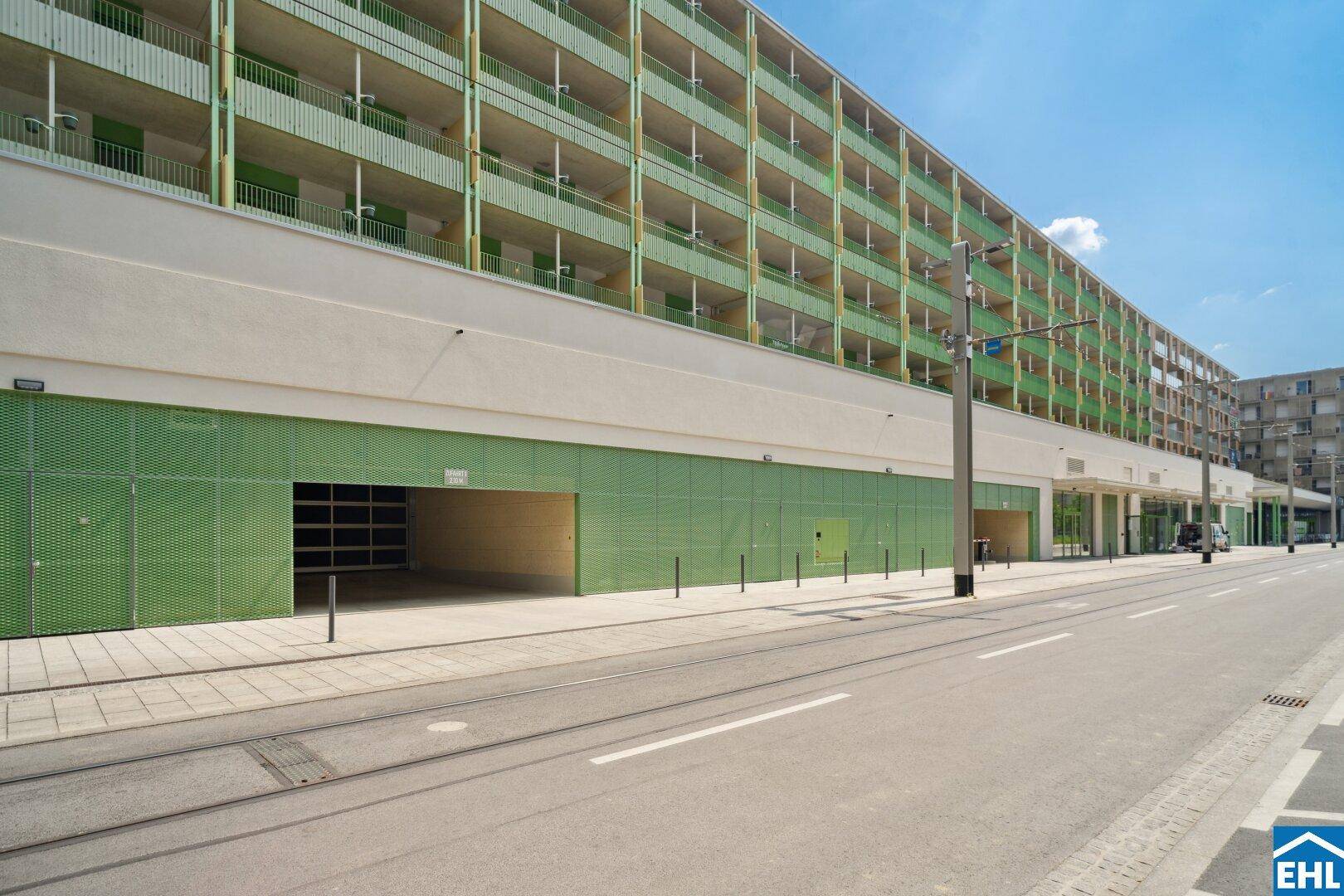 Ansicht eines modernen Gebäudes mit grüner Fassade und Tiefgarageneinfahrt an der Straße.