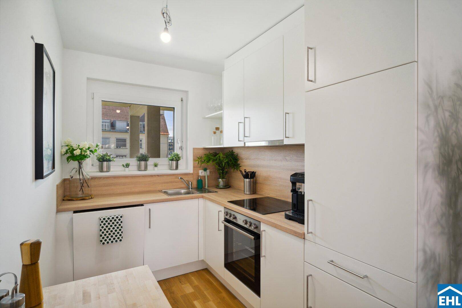 Moderne Einbauküche mit weißen Schränken, Holzarbeitsplatte und Fenster.
