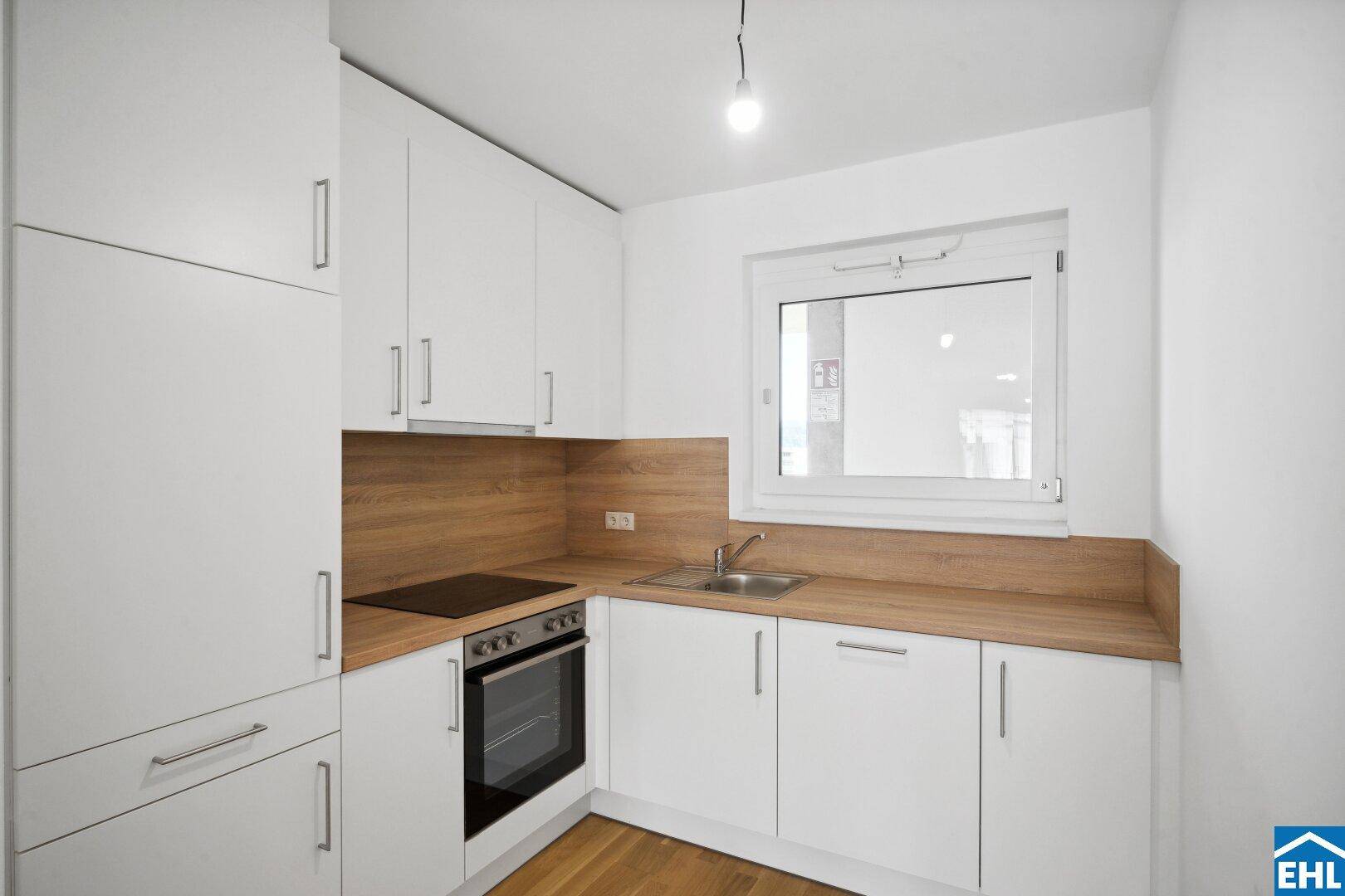 Moderne Einbauküche mit weißen Schränken, Holzarbeitsplatte und Fenster, bereit zur Nutzung.