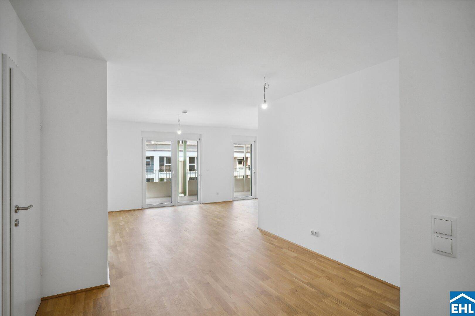 Geräumiger Wohnbereich mit Holzboden und zwei Balkonzugängen, bietet viel natürliches Licht.