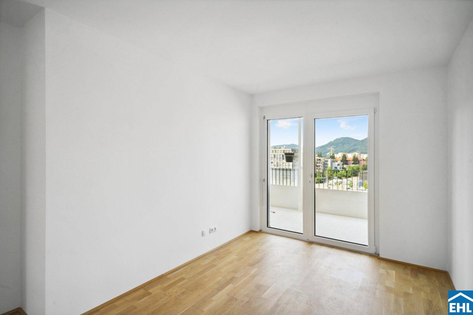 Helles Zimmer mit Holzboden und Zugang zu einem Balkon mit Bergblick.