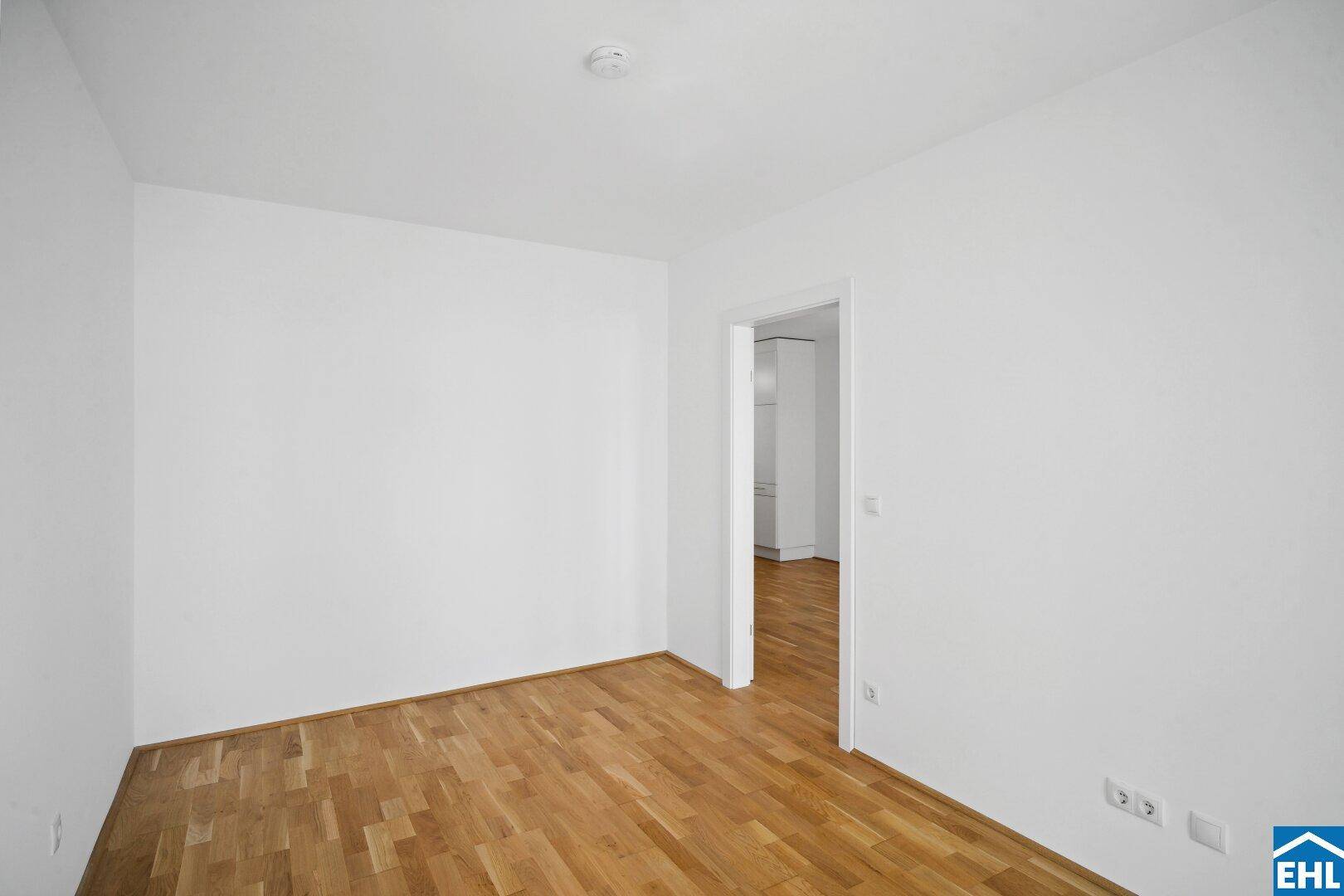 Leeres Zimmer mit Parkettboden und weiß gestrichenen Wänden, bereit zur Einrichtung.