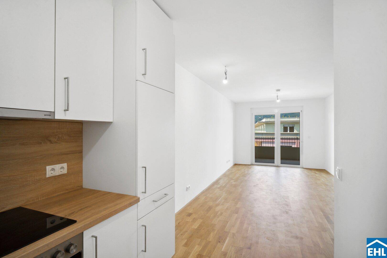 Heller offener Wohnbereich mit Holzboden und Zugang zu einem Balkon, bereit zur Einrichtung.