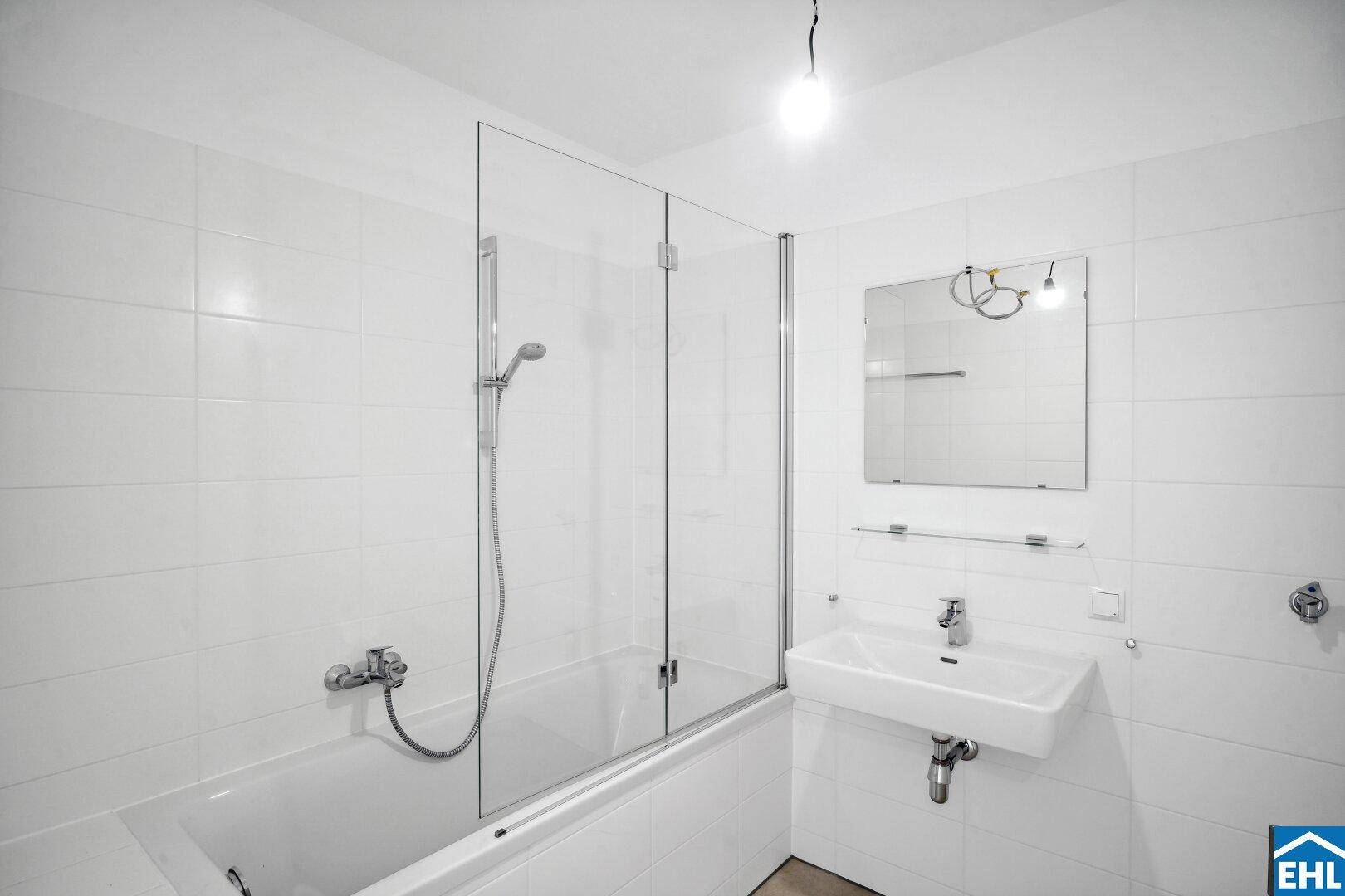 Helles Badezimmer mit Badewanne, Duschwand aus Glas und weiß gefliesten Wänden.