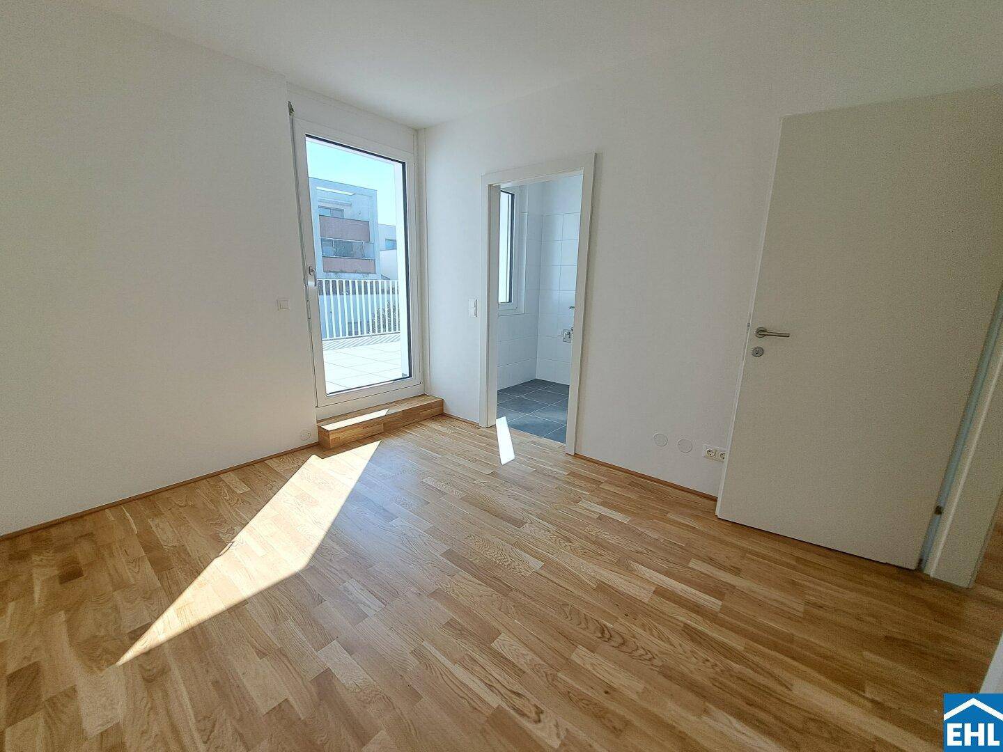 Helles Schlafzimmer mit Parkettboden, Zugang zur Terrasse und angrenzendem Badezimmer.