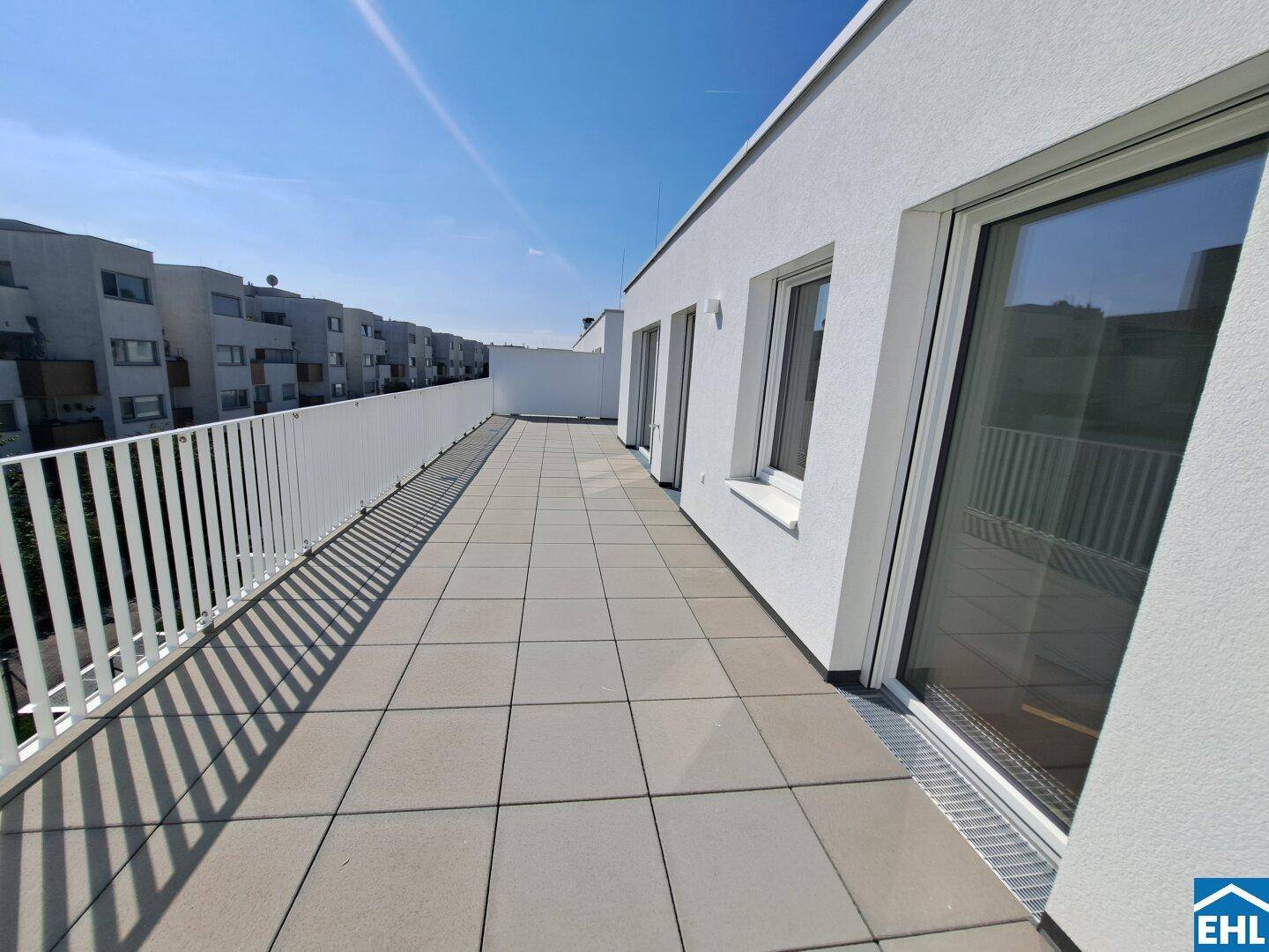 Lange, geflieste Terrasse mit weißem Geländer und mehreren Zugängen zu den Innenräumen.