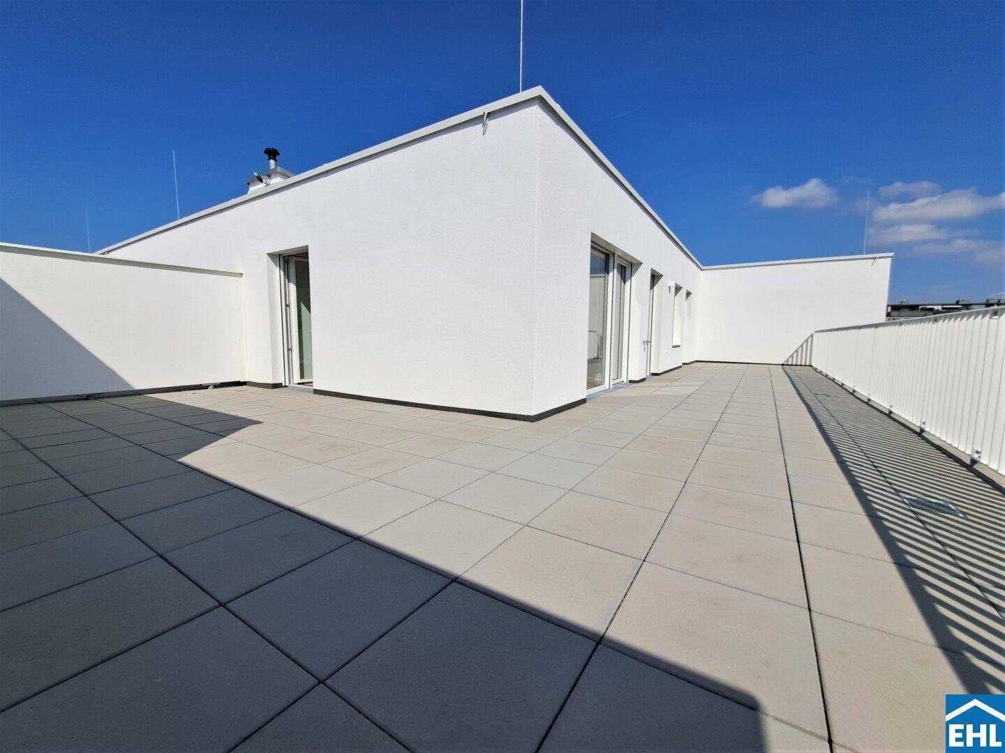 Großzügige, sonnige Dachterrasse mit modernen Fliesen und weißem Geländer.