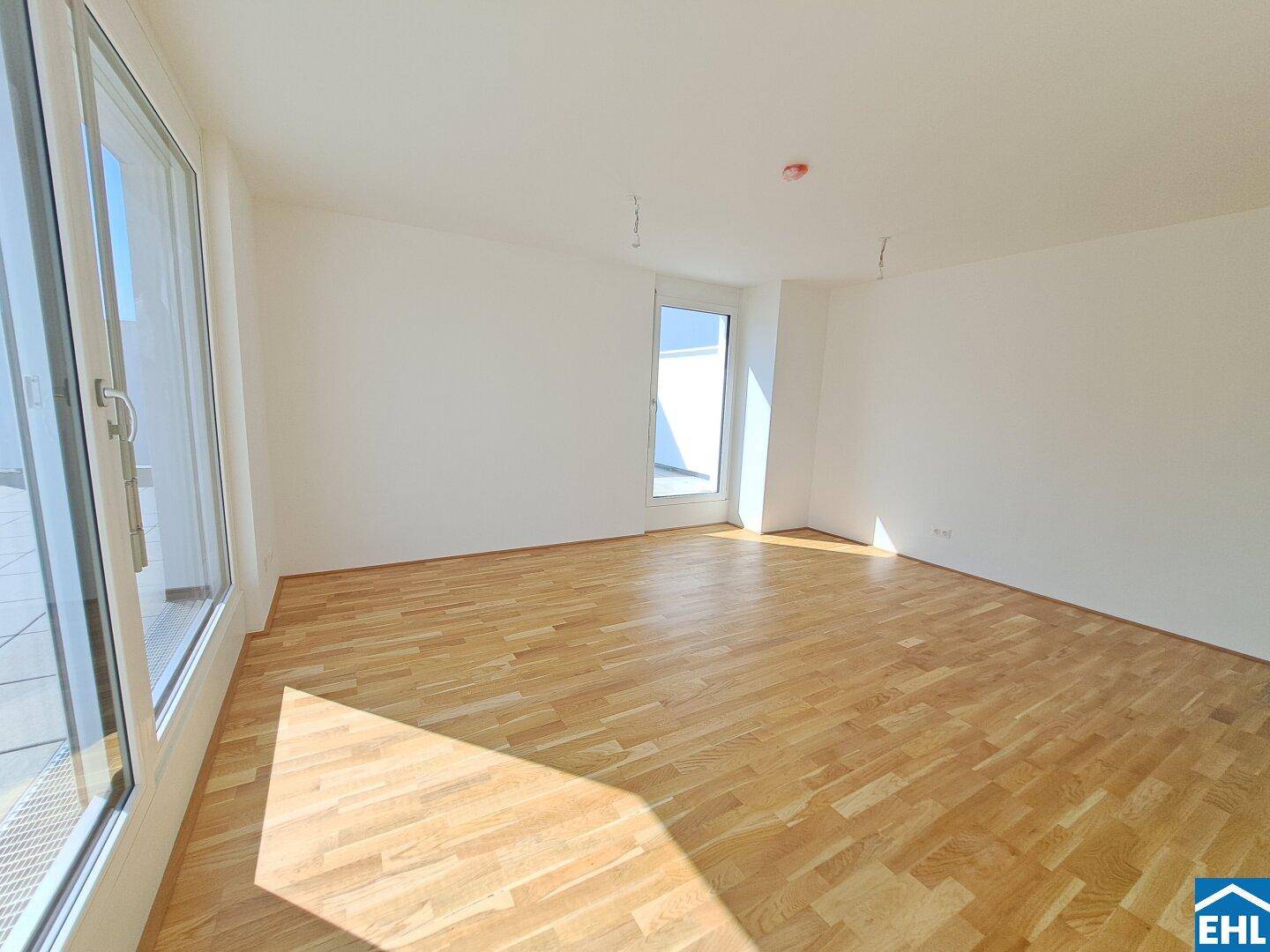 Heller Wohnraum mit Parkettboden und großen Fenstern, die den Zugang zur Terrasse ermöglichen.