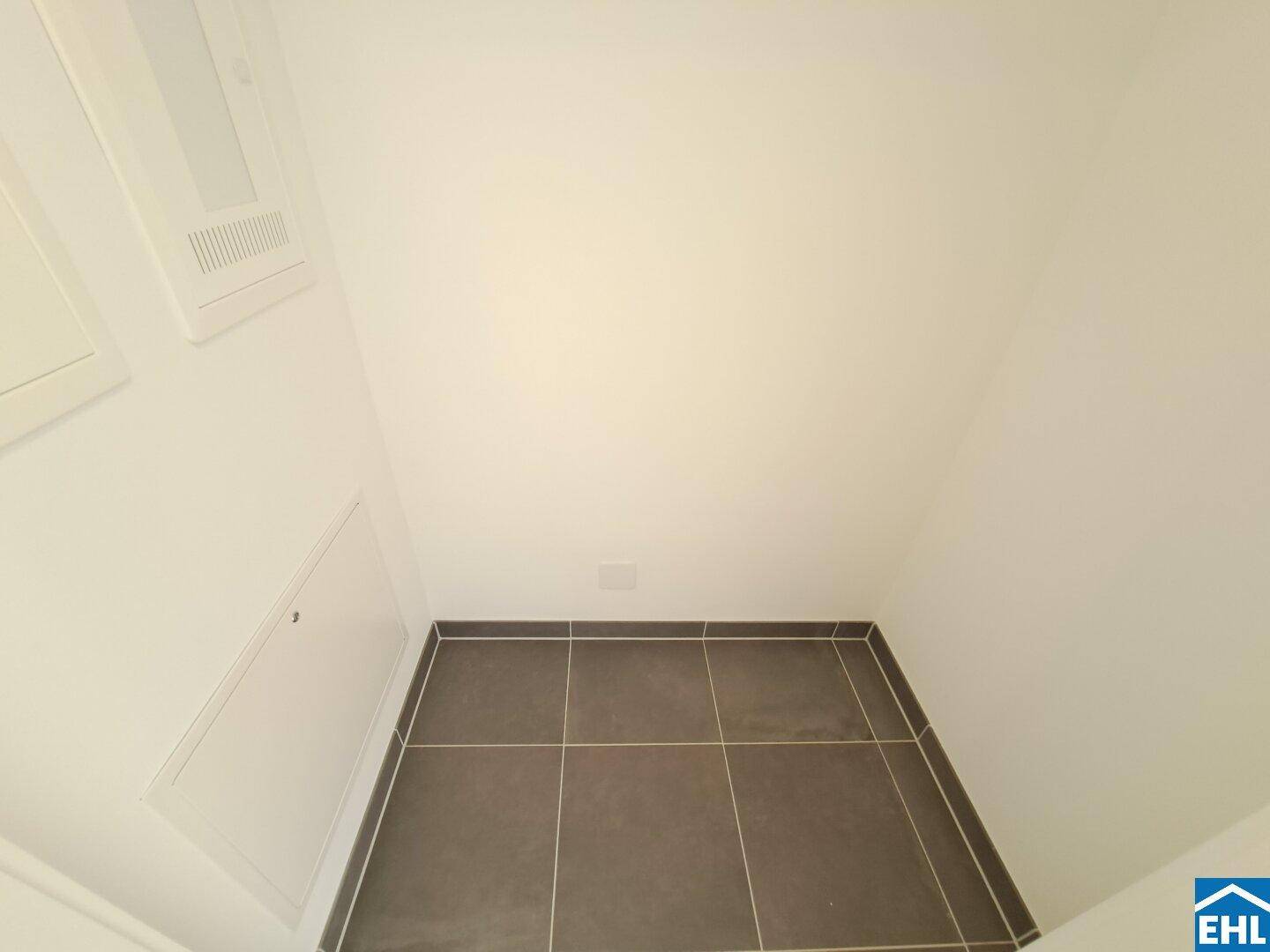 Kleiner Abstellraum mit dunklem Fliesenboden und weißen Wänden, ideal für Haushaltsgeräte.