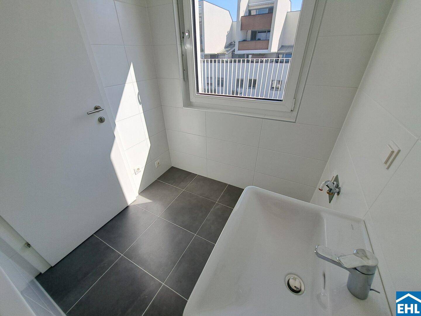 Helles Badezimmer mit modernen Fliesen, Waschbecken und Fenster für natürliche Belüftung.