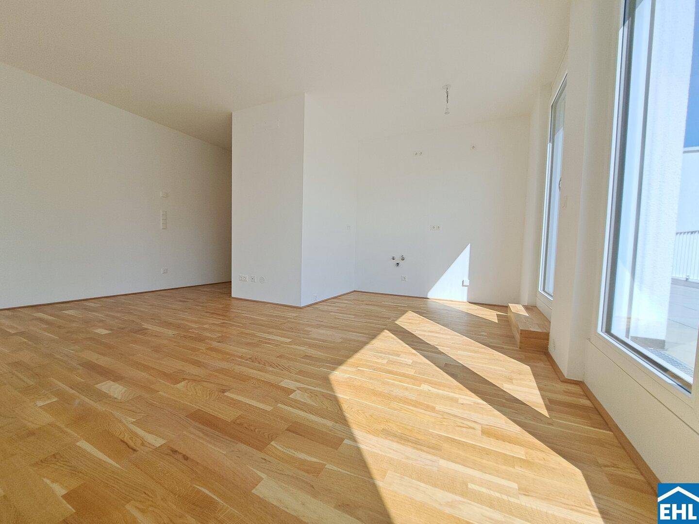 Lichtdurchfluteter Wohnraum mit hellem Parkettboden und weißen Wänden, bereit zur Einrichtung.