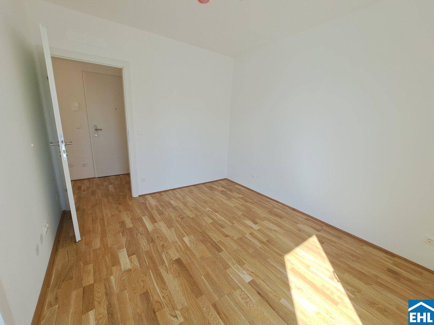Leeres Schlafzimmer mit hellem Parkettboden und weißen Wänden, bereit zur individuellen Gestaltung.
