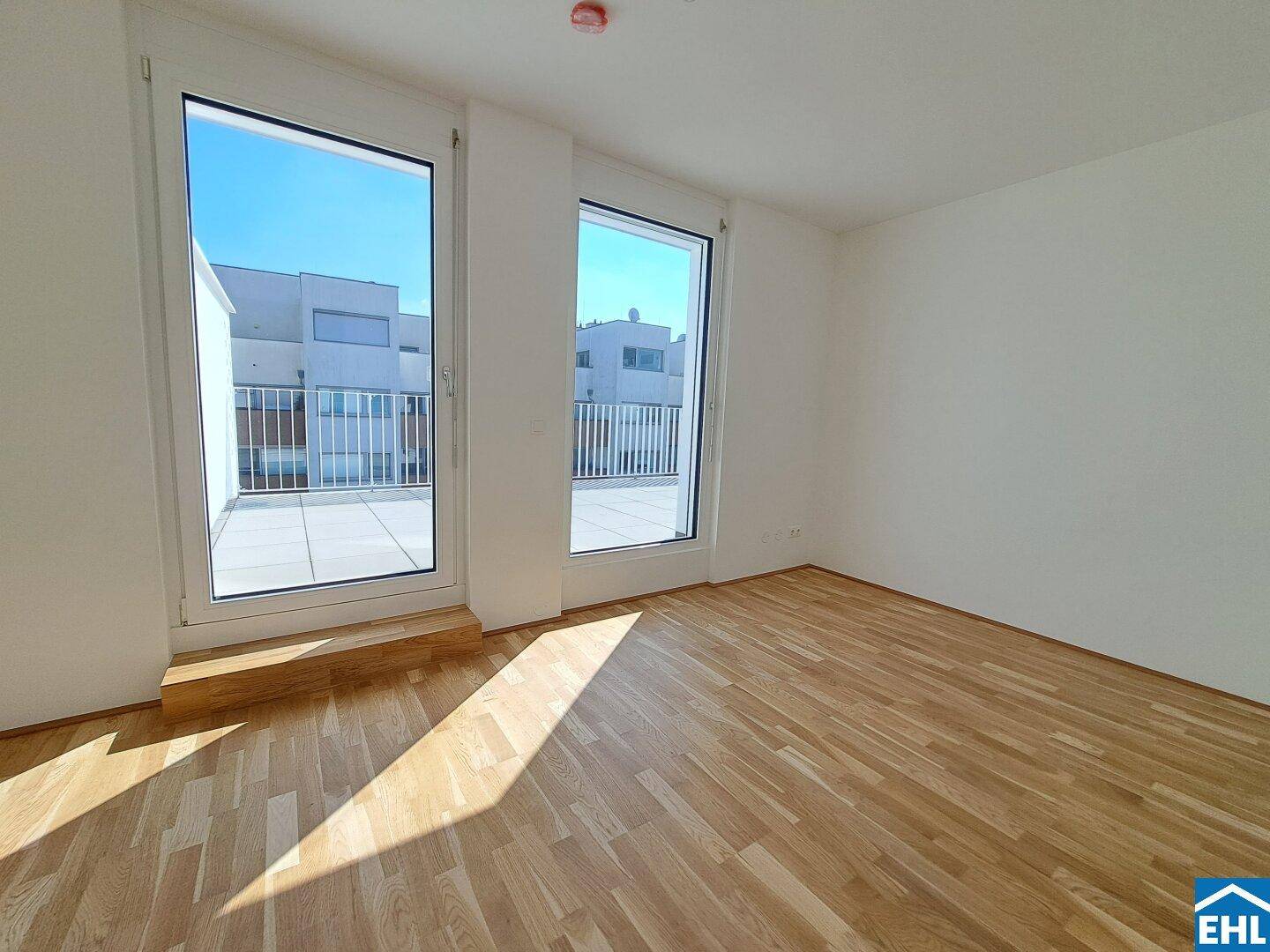 Lichtdurchflutetes Zimmer mit Holzboden und großen Fenstern, die viel Tageslicht hereinlassen.