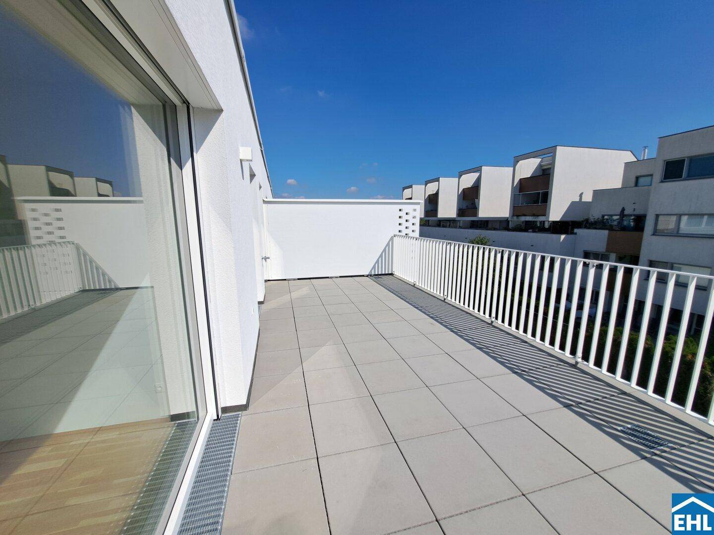 Sonnige Dachterrasse mit moderner weißer Brüstung und Blick auf die Nachbargebäude.