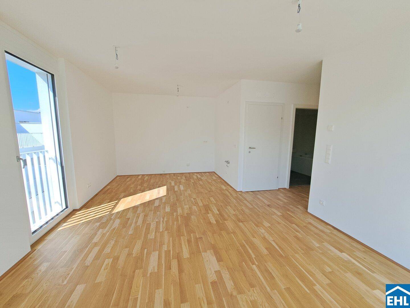 Geräumiger, heller Wohnraum mit Holzboden und Zugang zu einem Außenbereich.