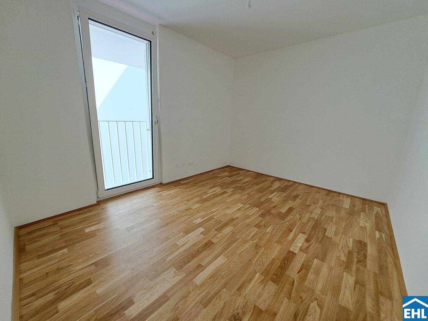 Helles Zimmer mit Holzboden und Zugang zu einem kleinen Balkon oder einer Loggia.