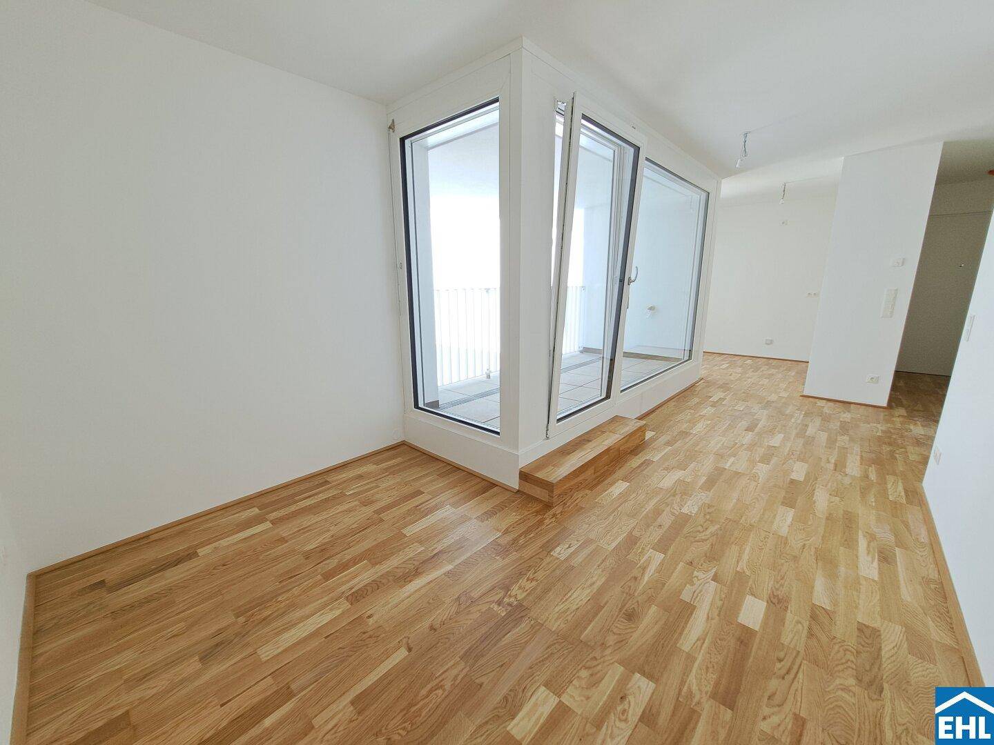 Lichtdurchfluteter Raum mit Eckfenstern und Holzboden in einem modernen Neubau.