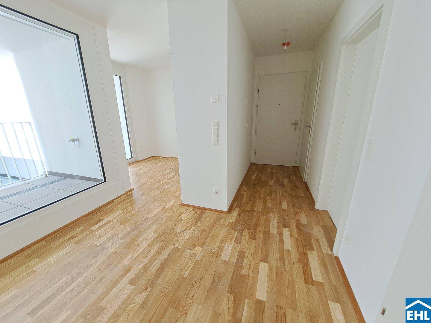 Heller Flur mit Holzboden und weiß gestrichenen Wänden, der zu den Wohnbereichen führt.