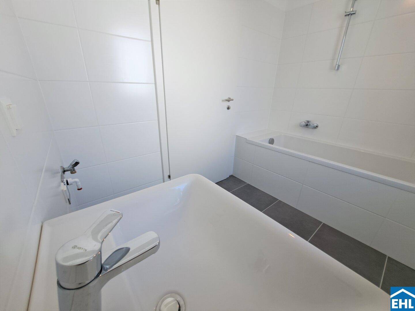 Modernes Badezimmer mit weiß gefliesten Wänden, Badewanne und dunklem Fliesenboden.