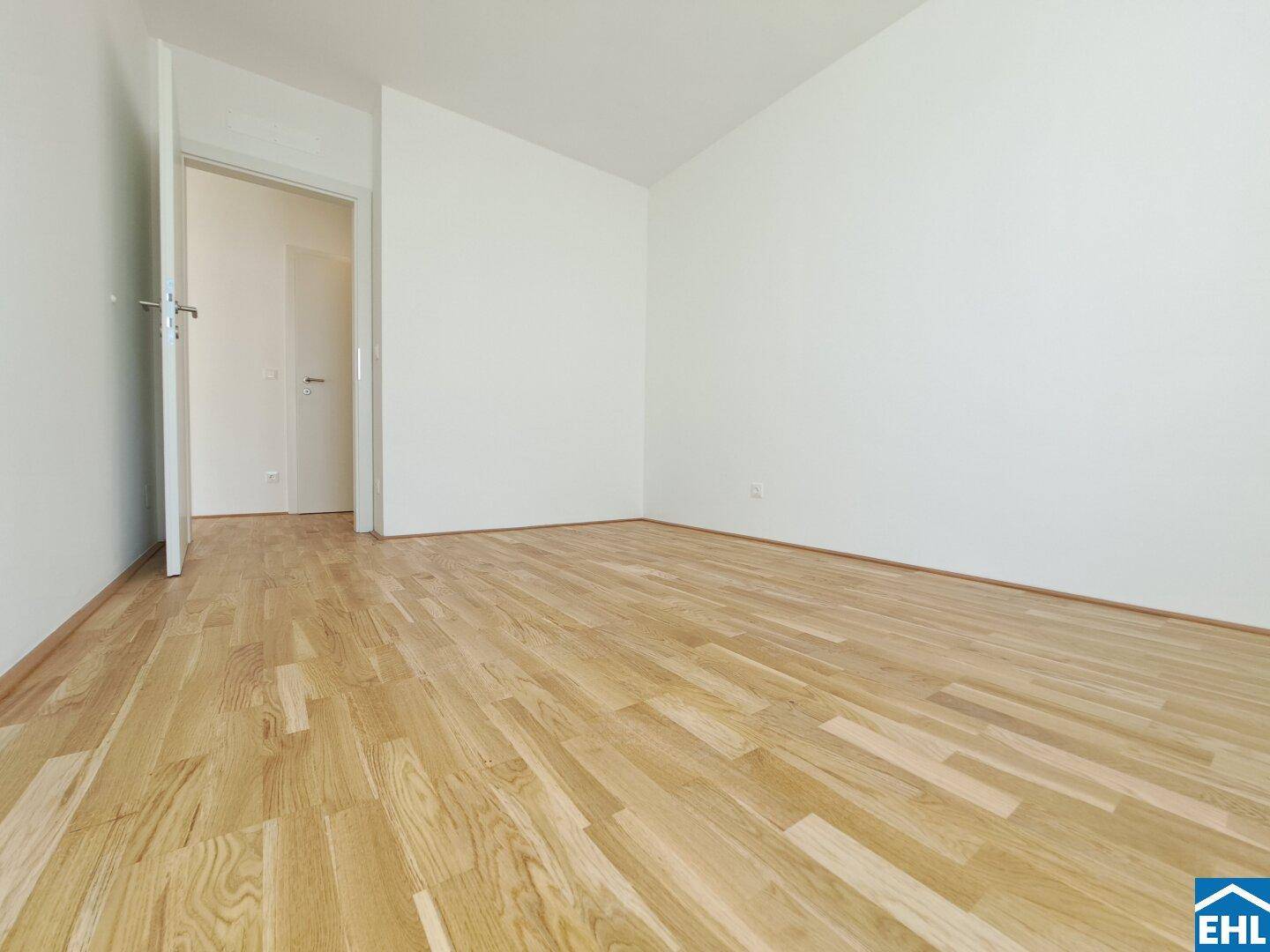 Helles, leeres Schlafzimmer mit Holzboden und weiß gestrichenen Wänden.