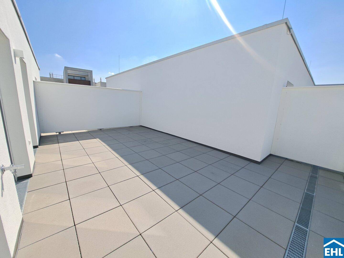 Großzügige, sonnige Dachterrasse mit hellen Fliesen und hohen Sichtschutzwänden.