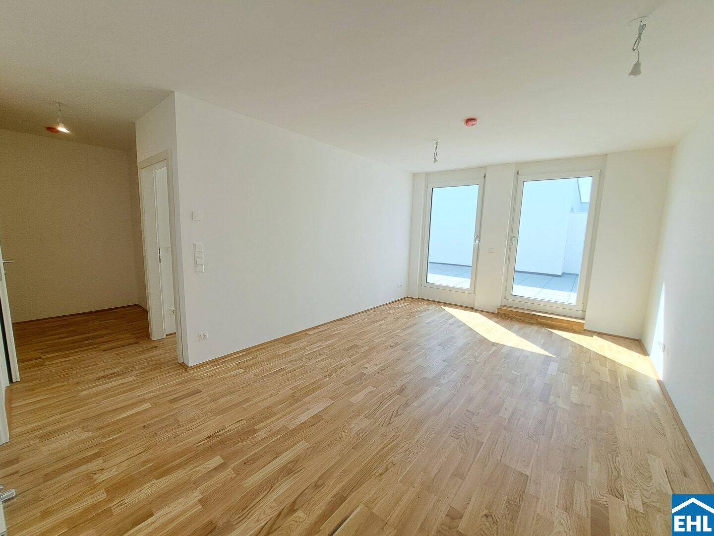 Lichtdurchfluteter Wohnbereich mit hellem Parkettboden und großen Fenstern zur Terrasse.