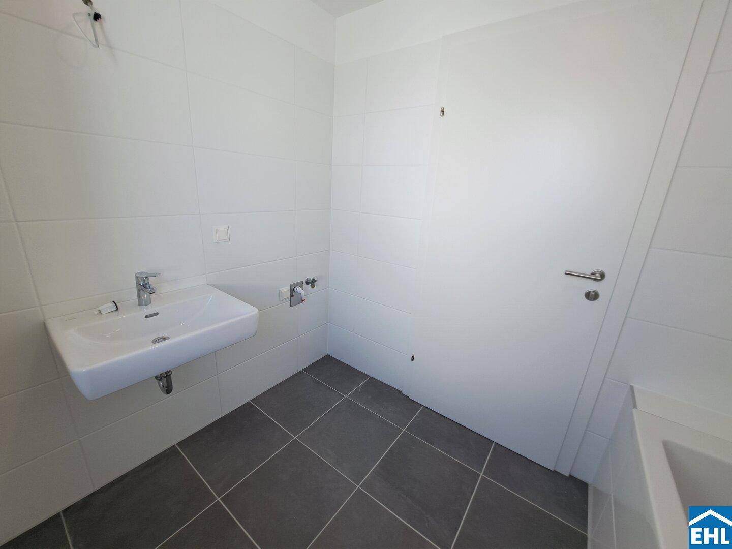 Helles Badezimmer mit weißem Waschbecken, modernen Armaturen und grauen Bodenfliesen.