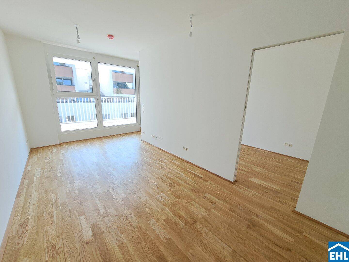 Lichtdurchfluteter Wohnbereich mit hellem Holzparkett und großem Fenster zum Balkon.