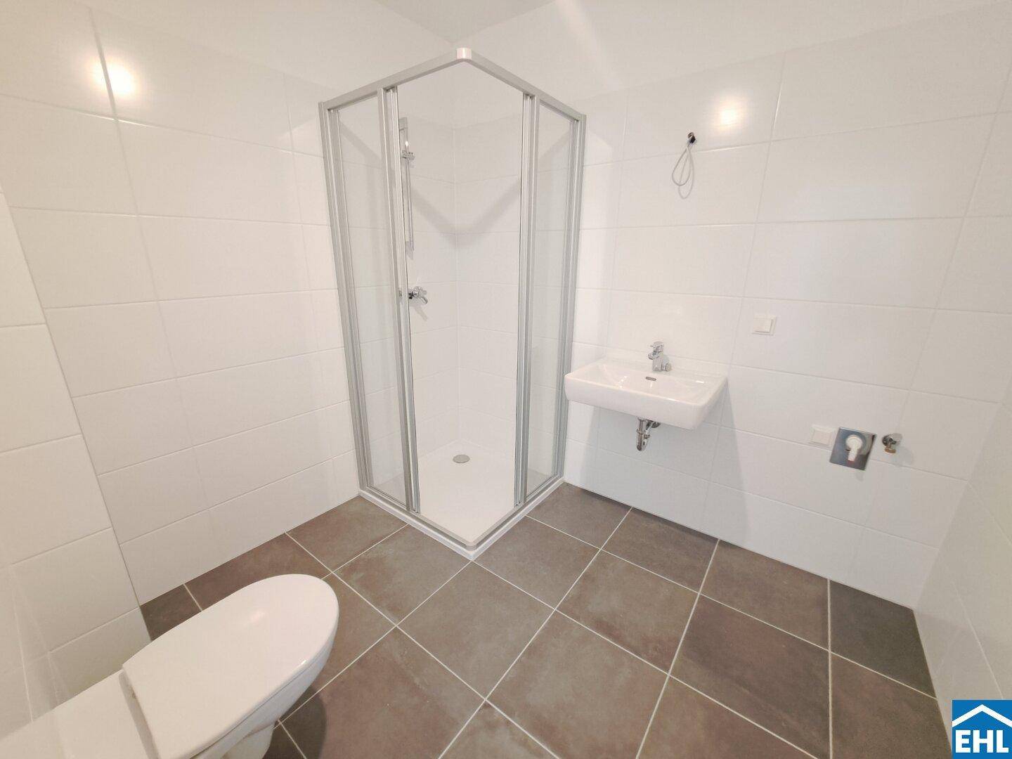 Modernes Badezimmer mit weiß gefliesten Wänden, dunklem Boden und Duschkabine.