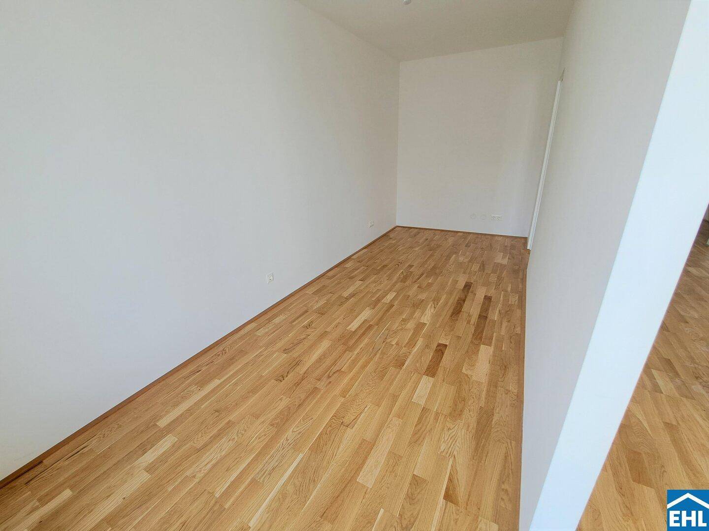Unmöblierter Raum mit sauberem Holzparkettboden und hellen, weißen Wänden.