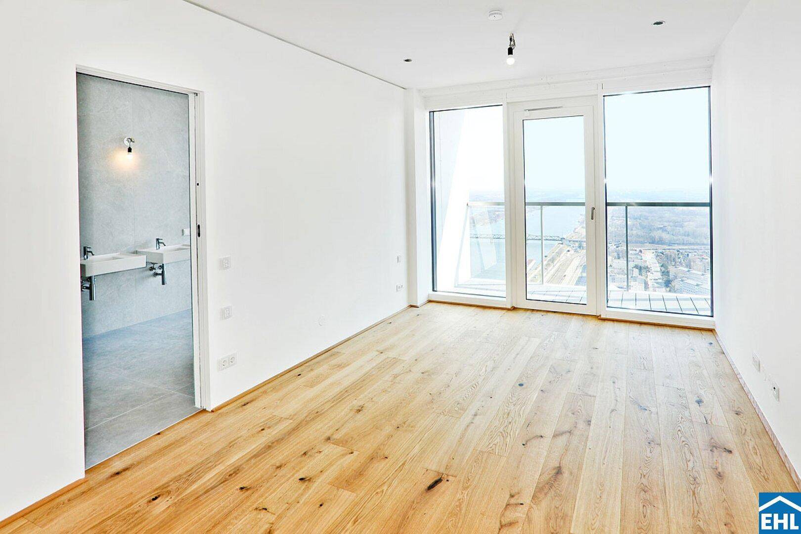 Geräumiges Schlafzimmer mit Holzboden und Zugang zu einem modernen Badezimmer.
