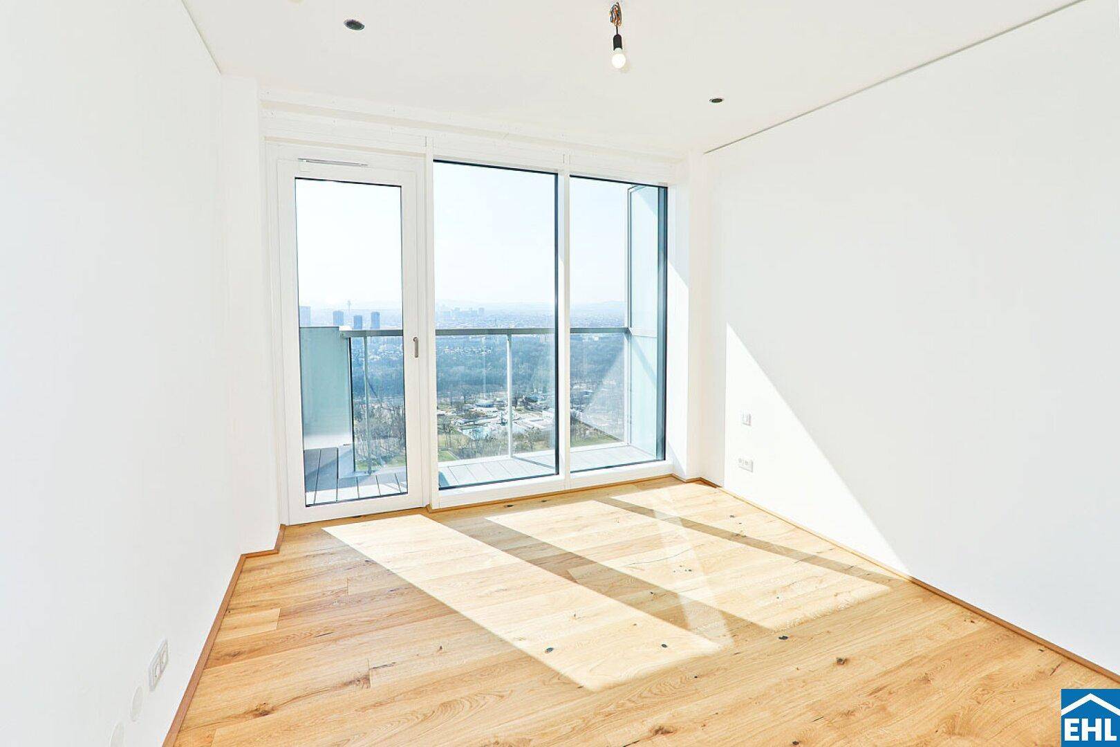 Helles Zimmer mit Holzboden und großem Fenster, das Zugang zu einem französischen Balkon bietet.