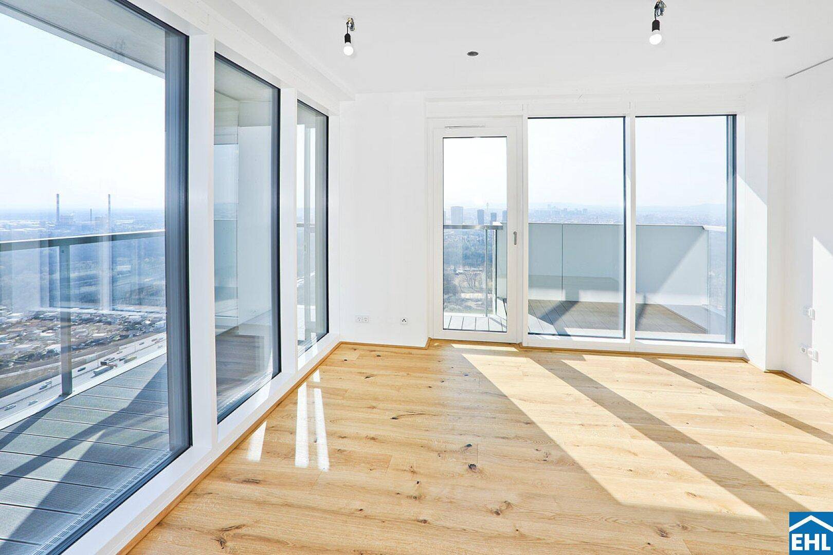 Lichtdurchfluteter Raum mit Holzboden und raumhohen Fenstern, die einen weiten Ausblick ermöglichen.