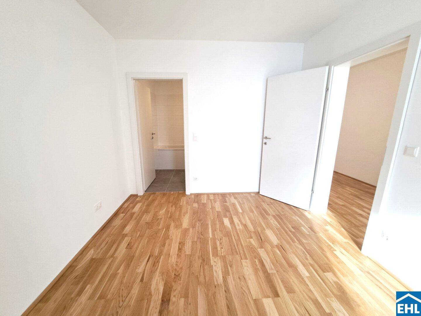 Leeres Zimmer mit Parkettboden und Zugang zu einem gefliesten Bereich.