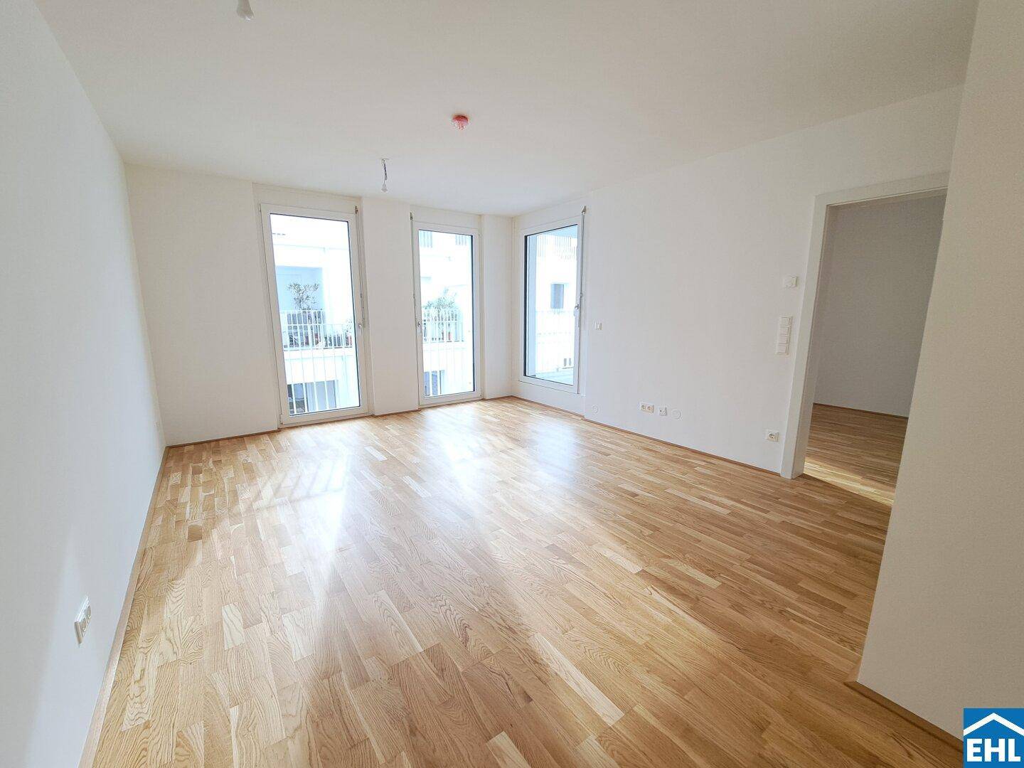 Lichtdurchflutetes Wohnzimmer mit hellem Parkettboden und Zugang zu Balkonen.