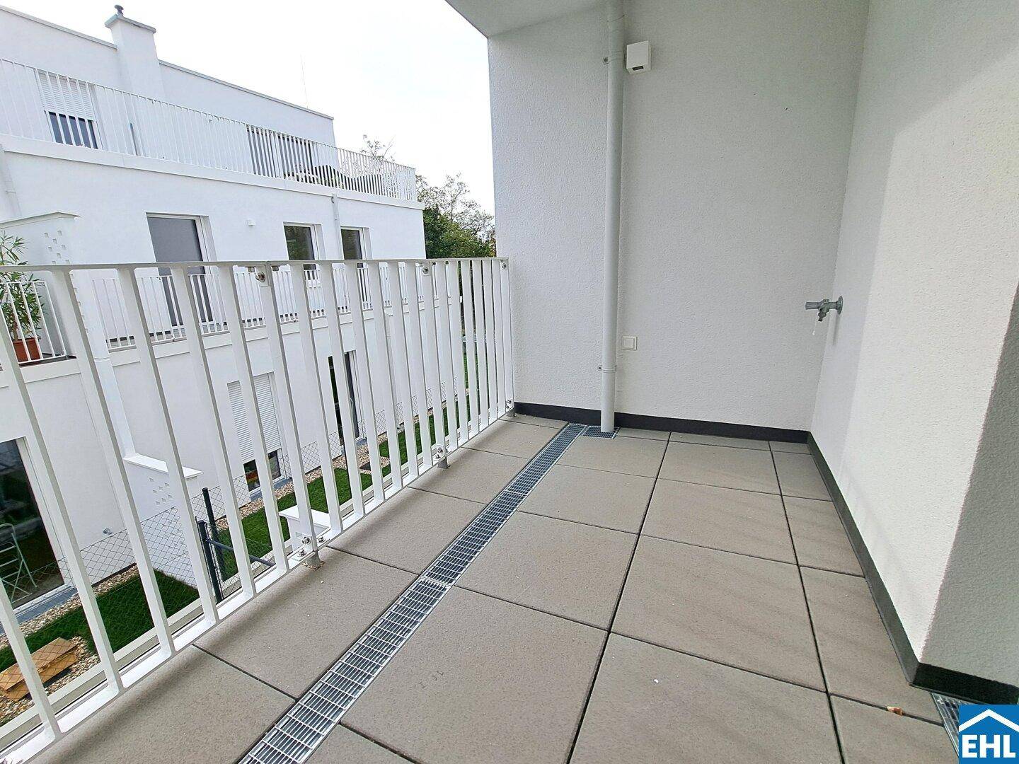 Geräumiger Balkon mit Fliesenboden und Blick auf die umliegenden Gebäude und Grünflächen.