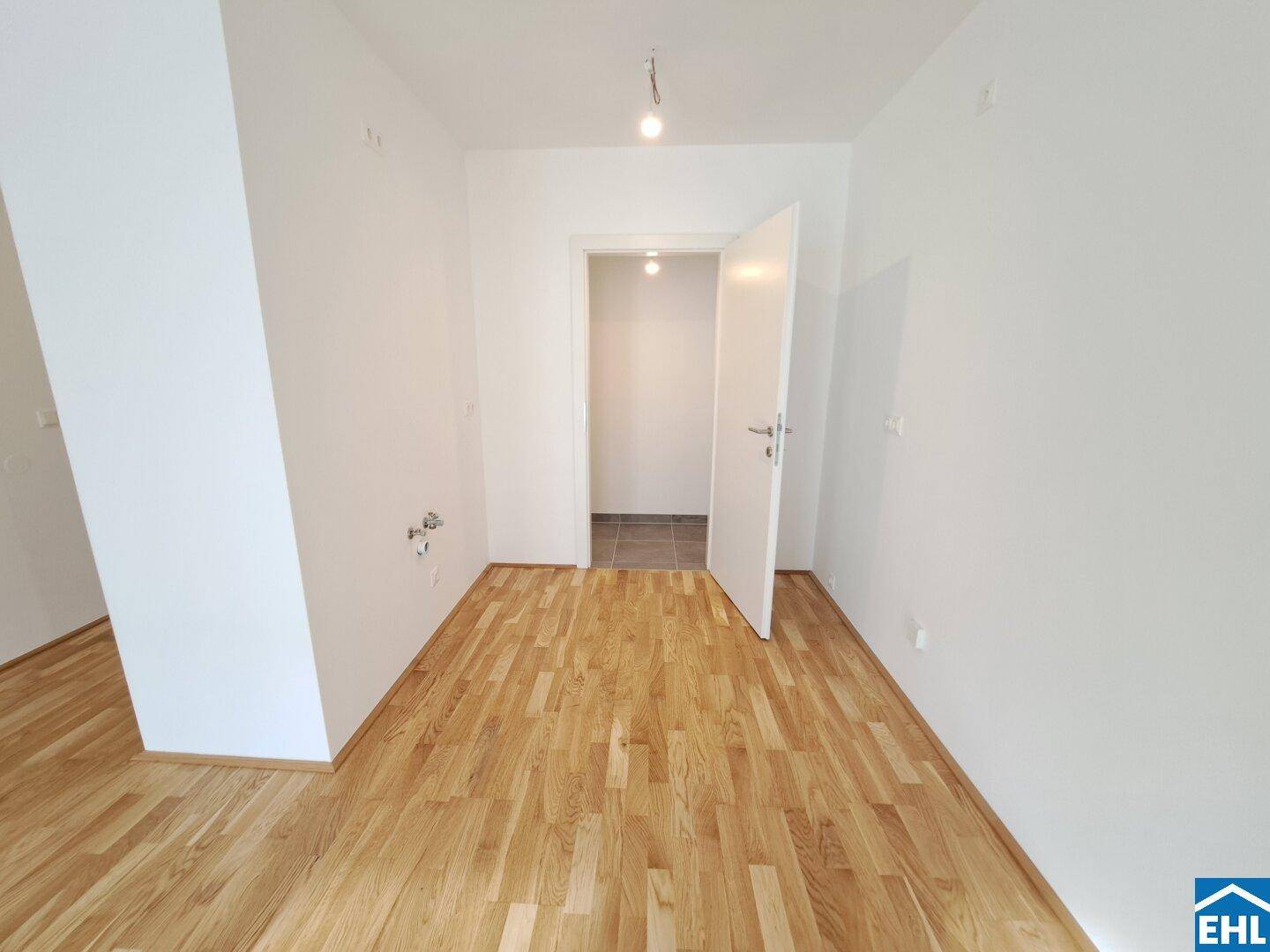 Heller Raum mit Parkettboden und Anschlüssen für eine Küche.