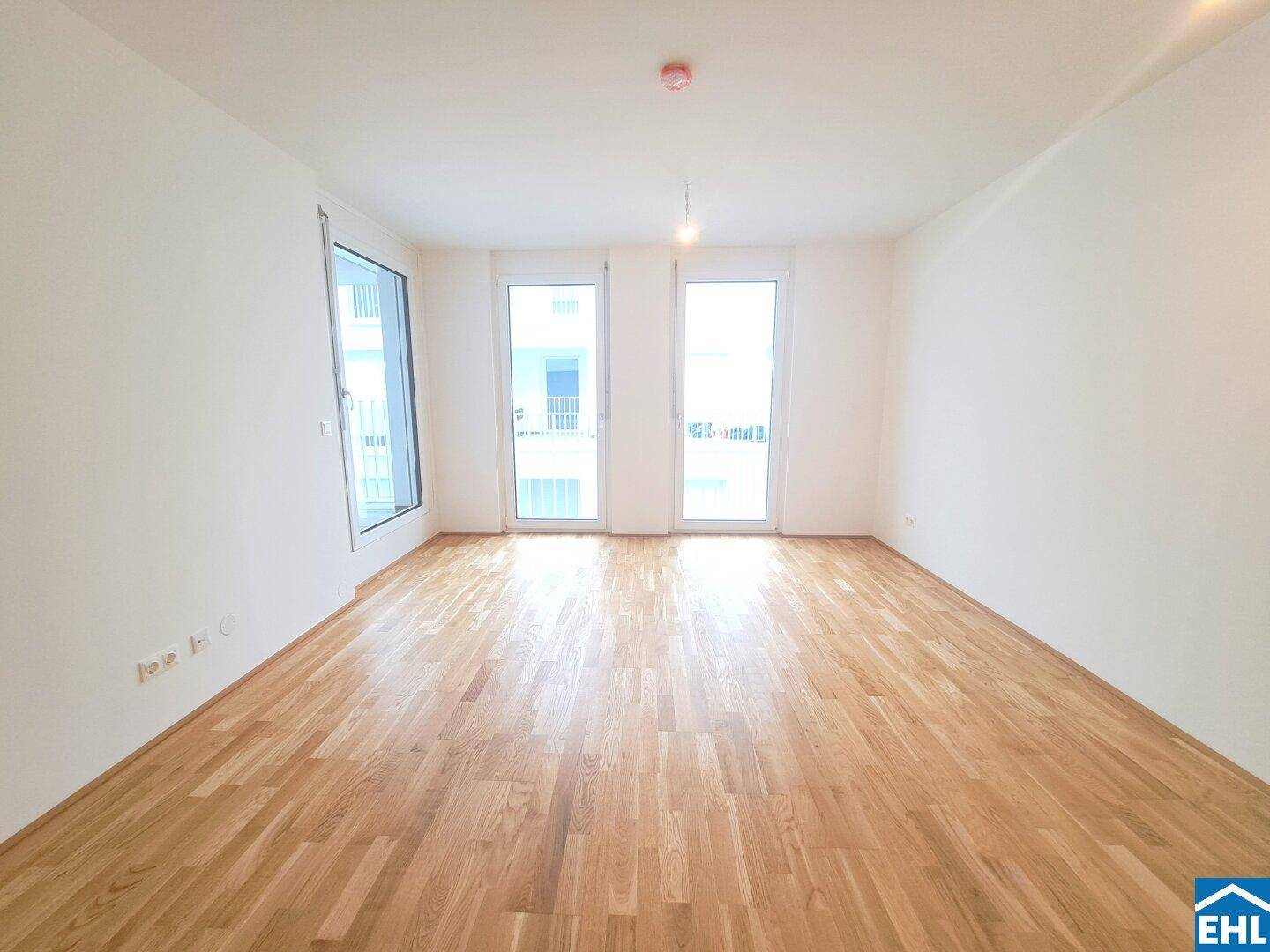 Lichtdurchfluteter Raum mit hellem Parkettboden und großen Fenstern zum Balkon.