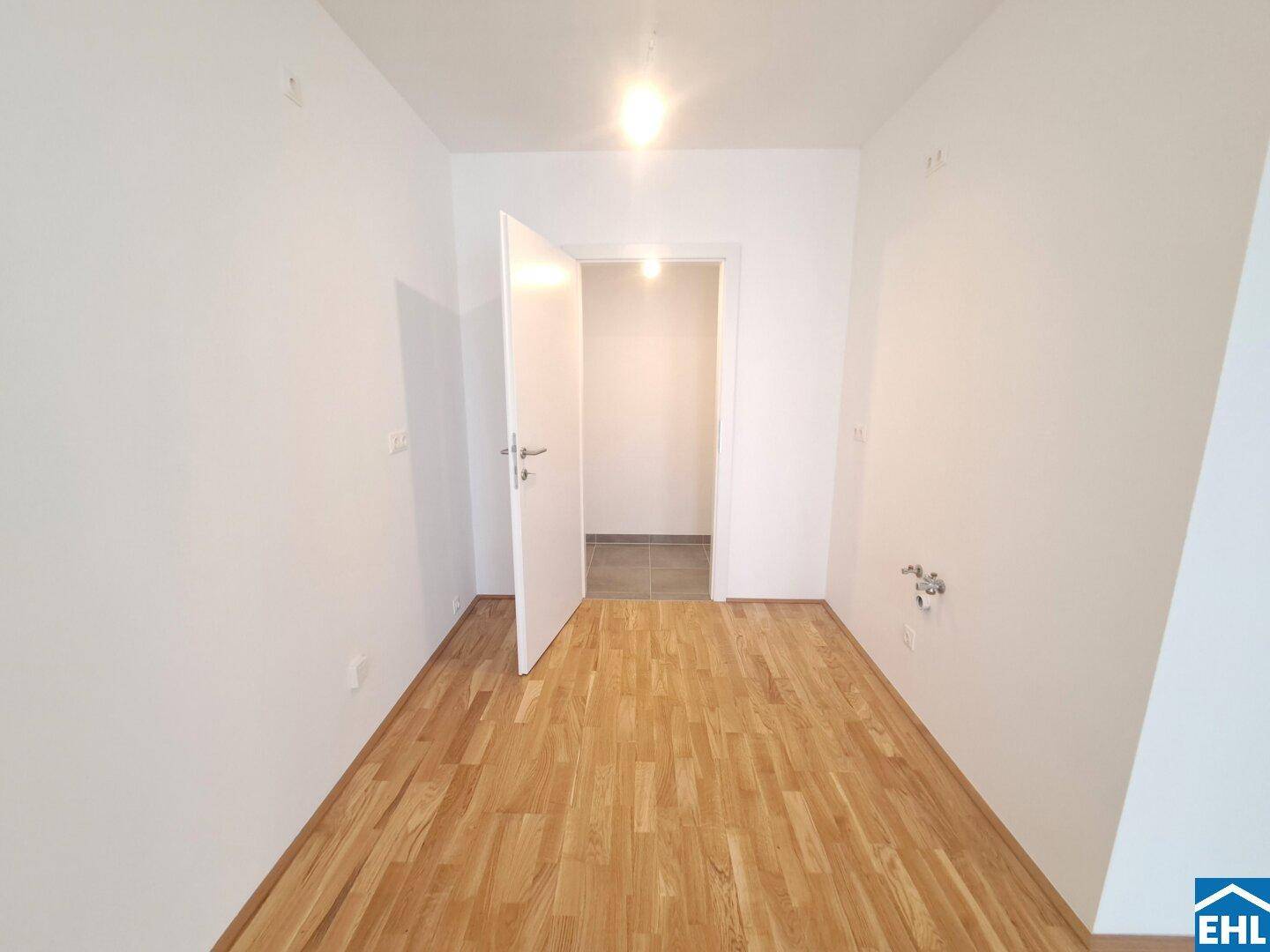 Kleiner, heller Raum mit Parkettboden und Zugang zu einem gefliesten Bereich.