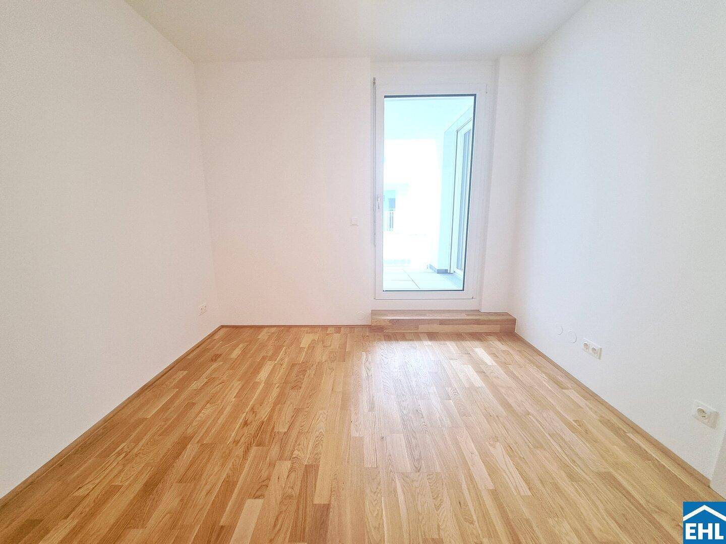 Heller Raum mit Holzboden und Zugang zu einem Außenbereich durch eine Glastür.