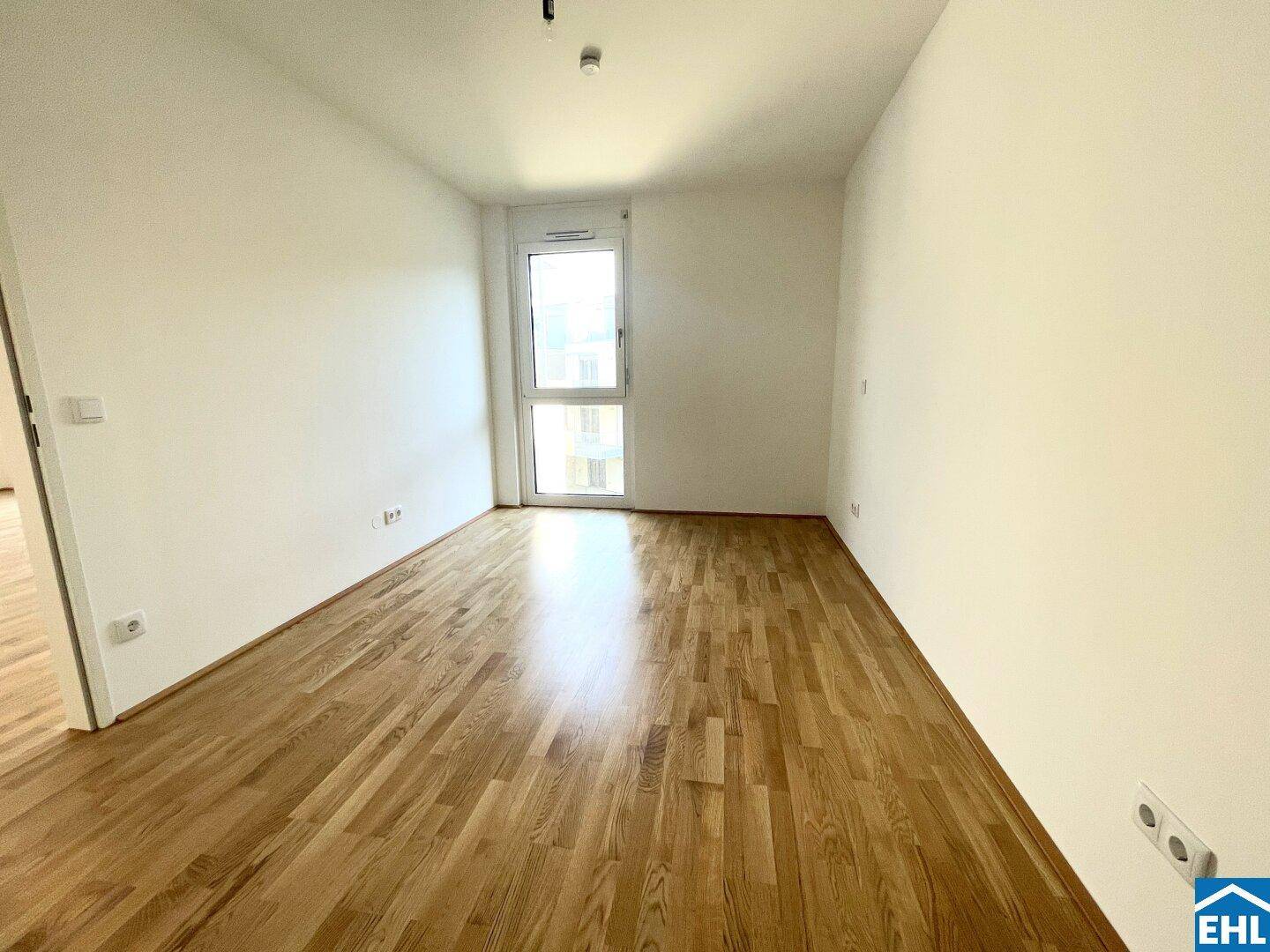 Helles Zimmer mit Parkettboden und einem großen Fenster, ideal als Schlaf- oder Arbeitszimmer.