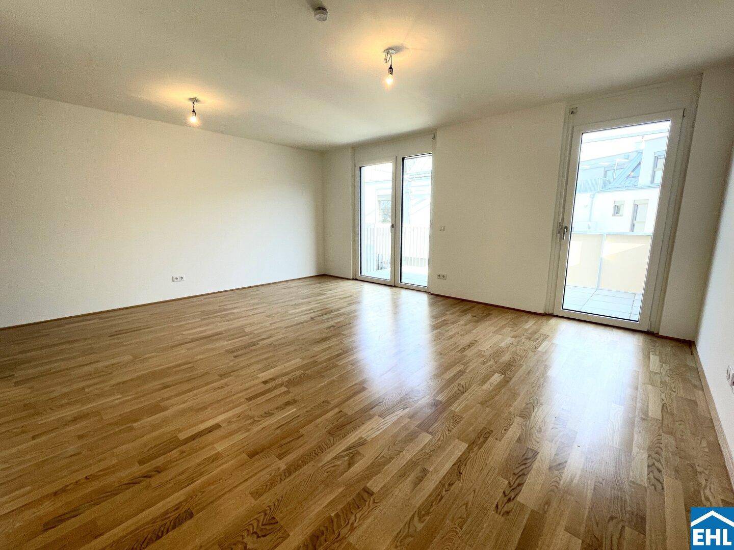 Geräumiges Wohnzimmer mit hellem Parkettboden und viel Tageslicht durch große Fenstertüren.