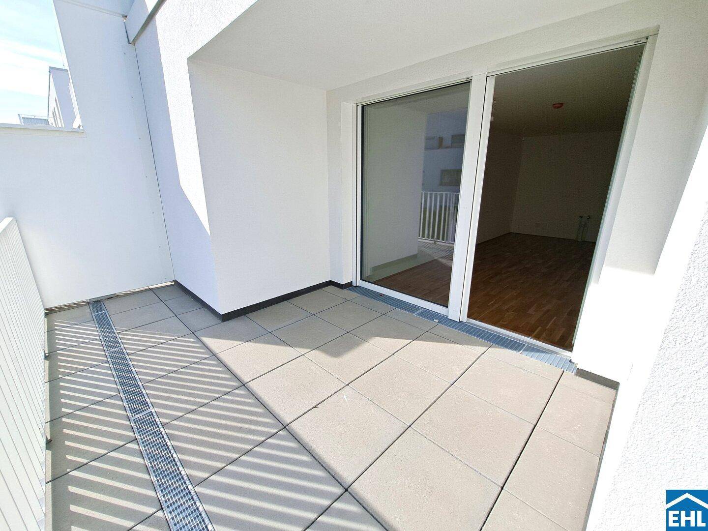 Moderner Balkon mit Fliesenboden und großer Glasschiebetür, die viel Licht hereinlässt.