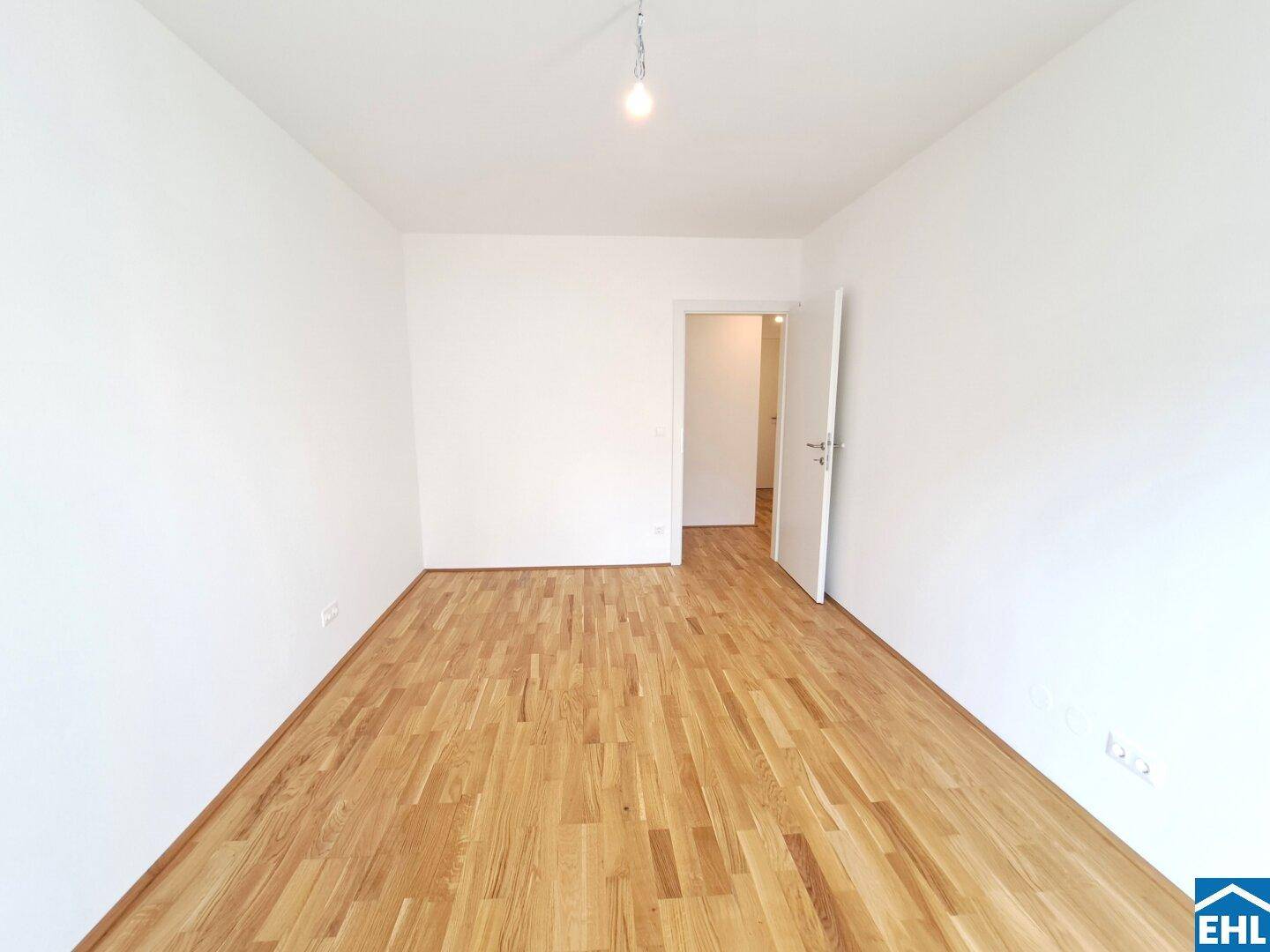 Geräumiges, leeres Schlafzimmer mit Holzboden und weiß gestrichenen Wänden.