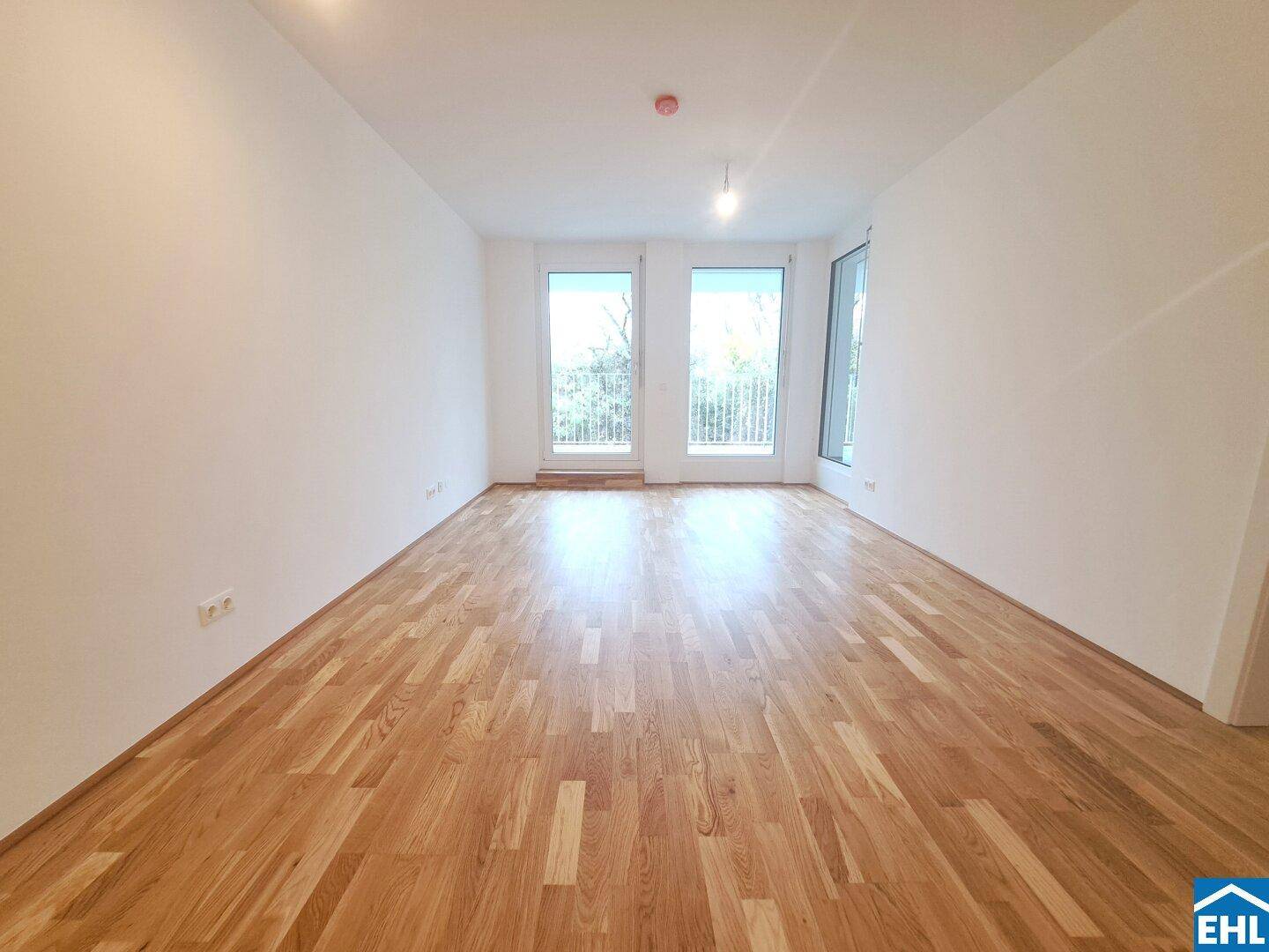 Lichtdurchfluteter Wohnbereich mit Holzboden und Zugang zu einem französischen Balkon.