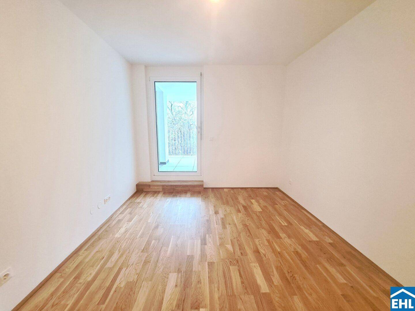 Leeres Schlafzimmer mit Parkettboden und direktem Zugang zu einem Balkon.